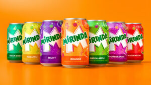 Various colorful varieties of Mirinda soda cans in front of orange background.